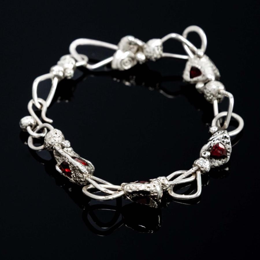 A silver bracelet with small red stones on a black reflective surface.
