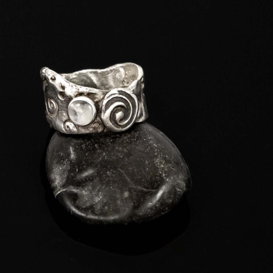 Photograph of a textured silver ring resting on a smooth dark stone against a black background.