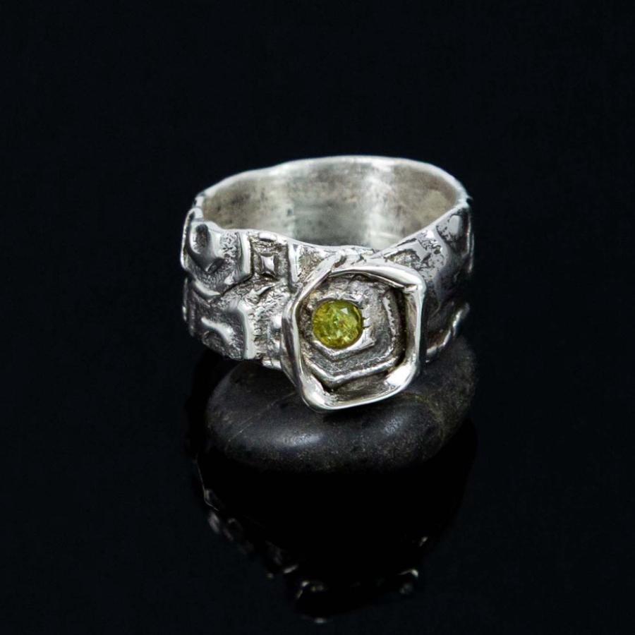 A silver ring with a small, round, green stone, resting on a black surface.
