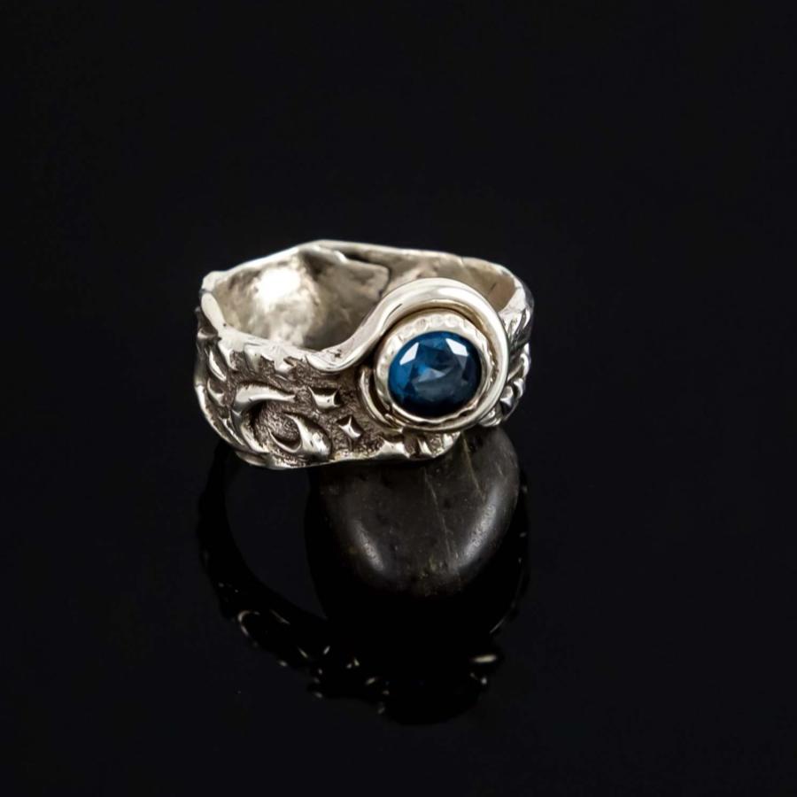 Photograph of a silver ring with a blue stone on a black reflective surface.