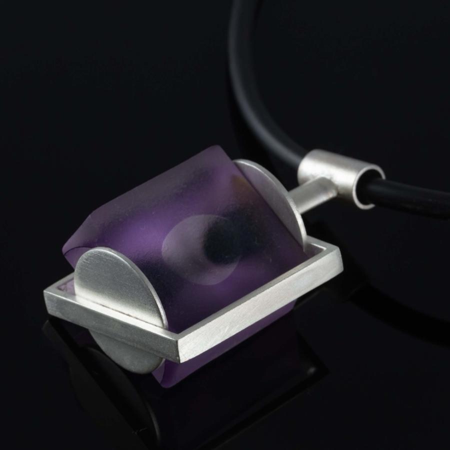 Photograph of a purple, rectangular pendant on a black cord against a black background.
