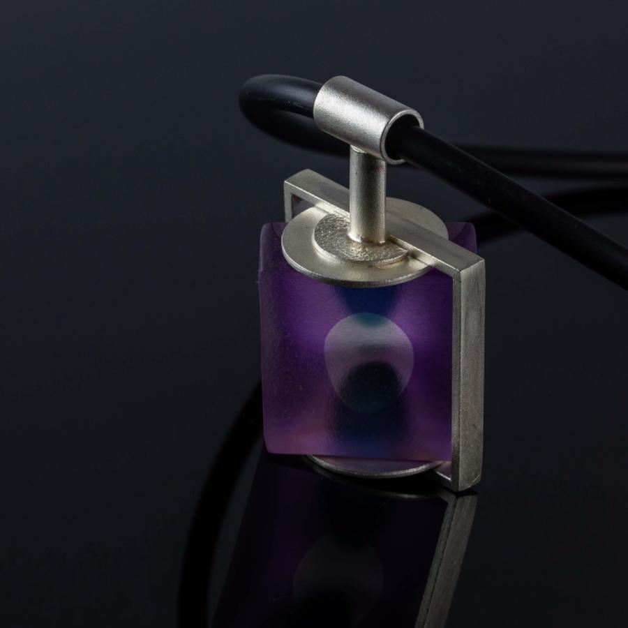 Photograph of a square purple glass pendant on a silver mount and black cord.