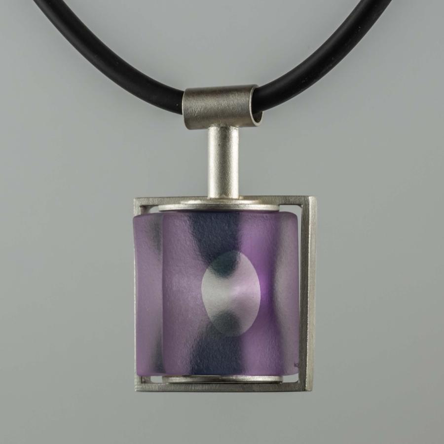 Photograph of a modern pendant with a purple glass cube set in a metal frame on a cord.