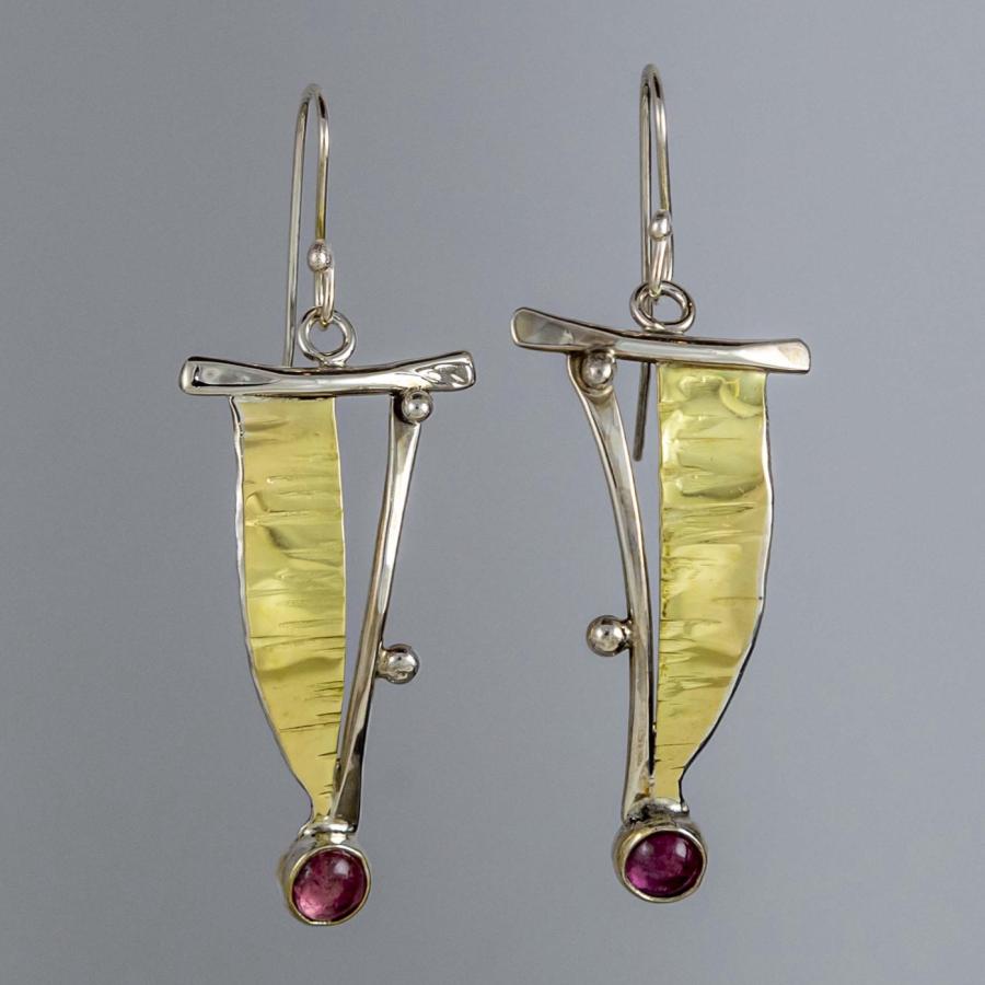 Photograph of silver and gold earrings with pink gemstone drops against a gray background.