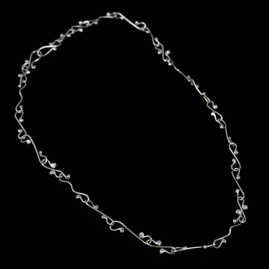 Silver necklace with decorative, intertwined links on a black background.