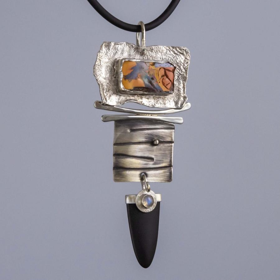 Artisan silver necklace pendant featuring a textured metal panel, an opal, and a black pointed stone.
