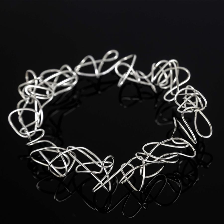 Photograph of a tangled silver wire bracelet on a black reflective surface.