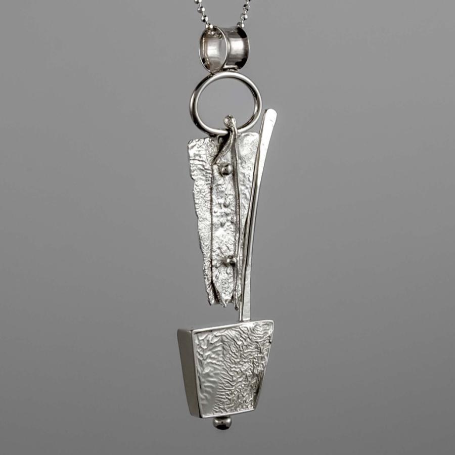 Silver pendant necklace with textured abstract geometric shapes on a gray background.