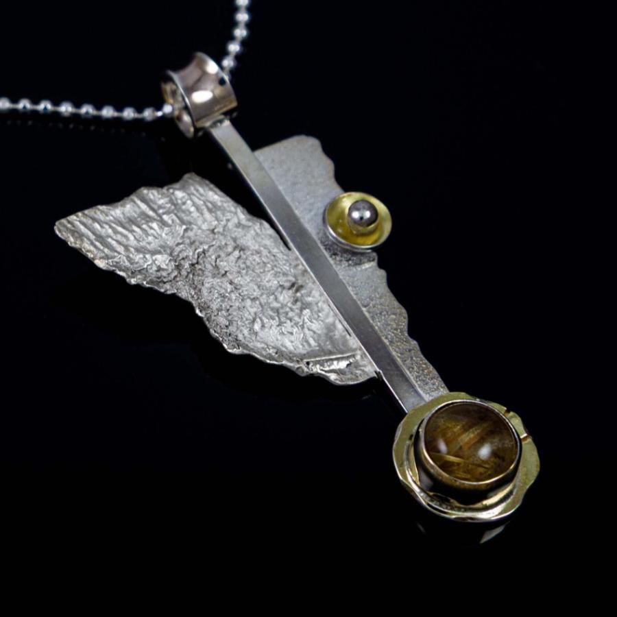 Photograph of a silver and gold abstract pendant necklace against a black background.