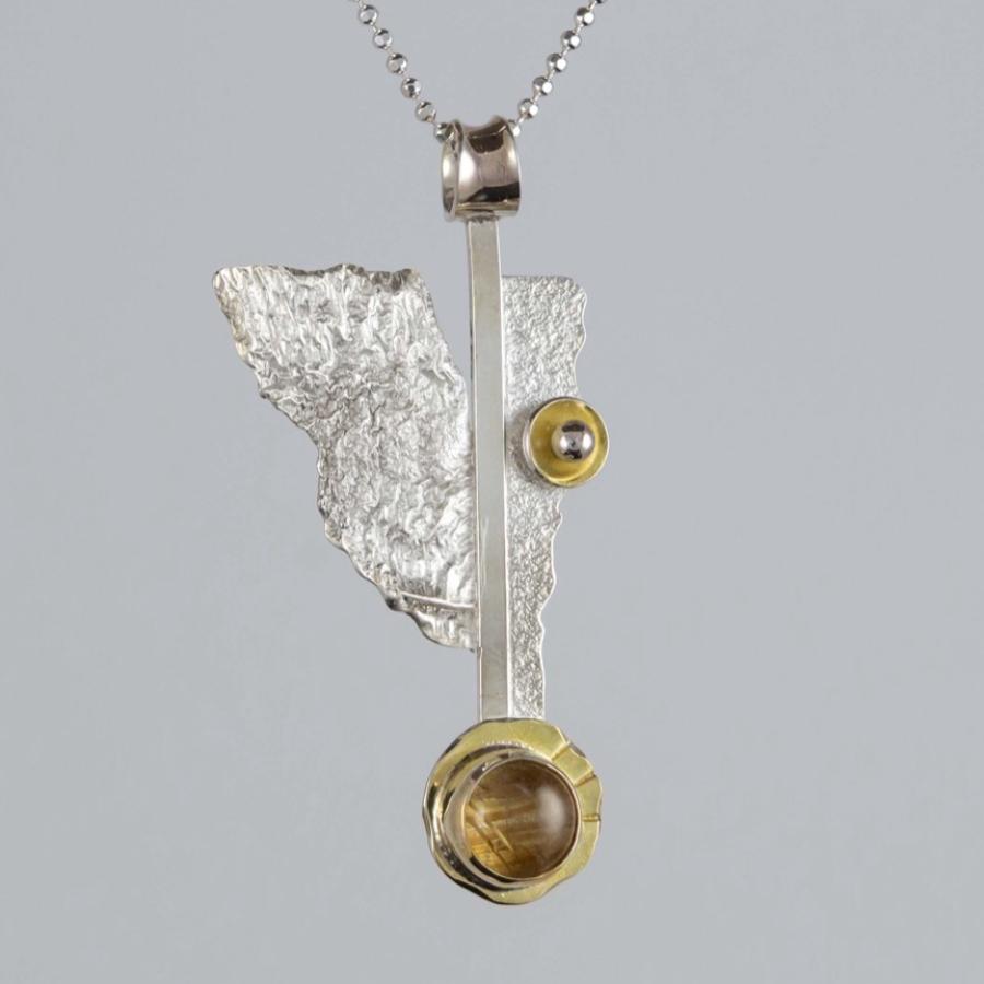 Photograph of a silver and gold abstract pendant on a delicate chain against a grey background.