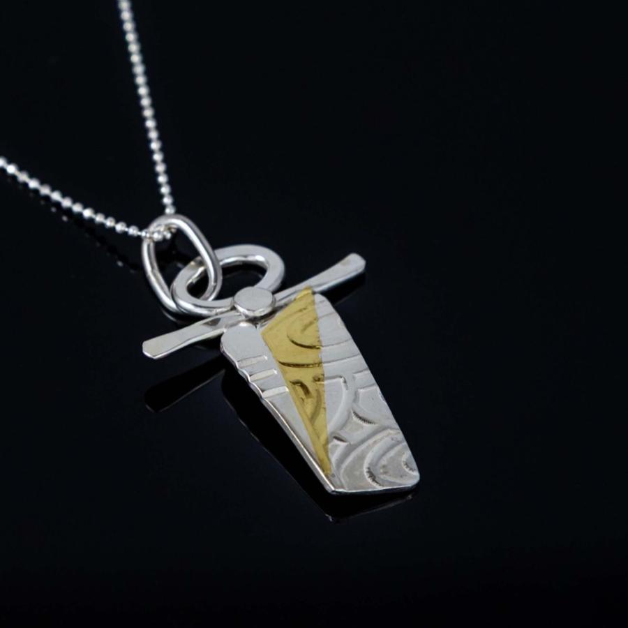 A silver necklace with a unique, textured silver and gold geometric pendant on a black background.