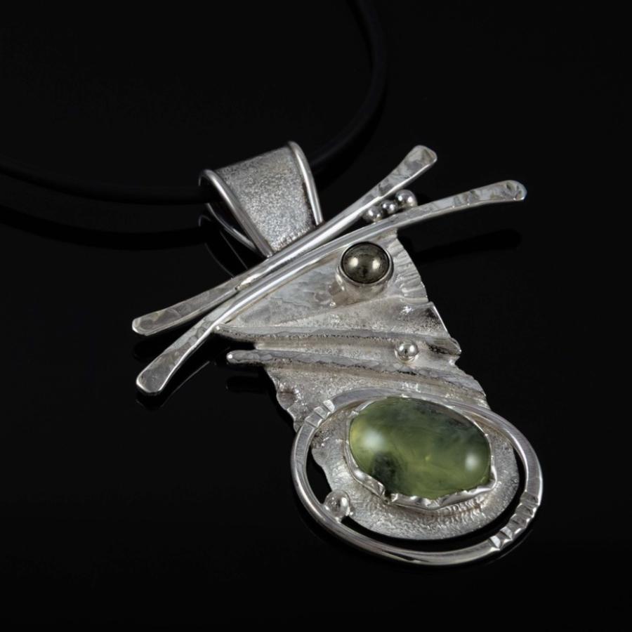 Photograph of an abstract silver pendant with a green gemstone on a black cord.