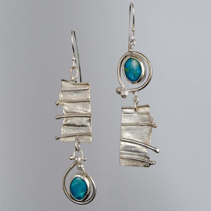 Photograph of two asymmetrical silver earrings with blue stones on a gray background.