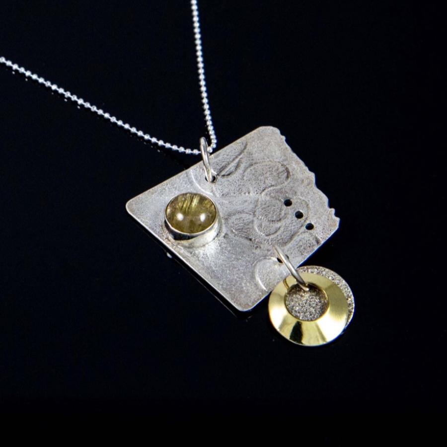 Silver necklace featuring a textured, angular pendant with gold accents and a gold colored stone.
