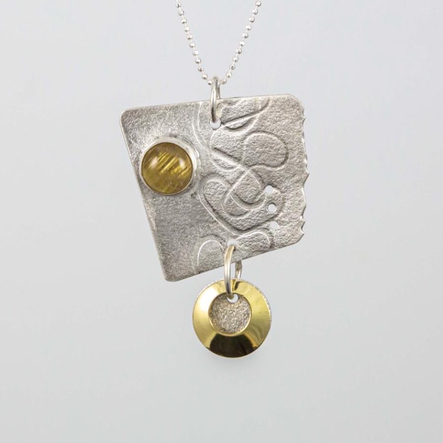 Photograph of a textured silver pendant with gold accents and a gold colored stone on a delicate chain.