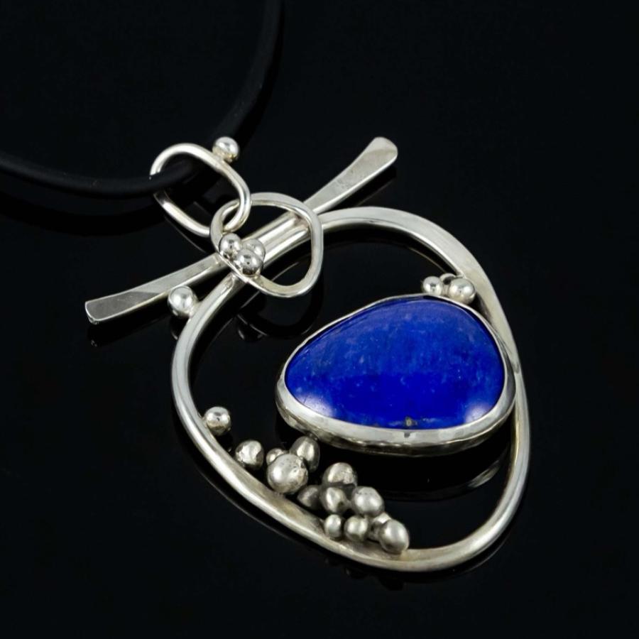 Photograph of a silver pendant featuring a blue lapis stone on a black cord.