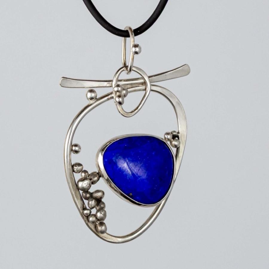 Photograph of a silver pendant with a blue stone on a black cord.