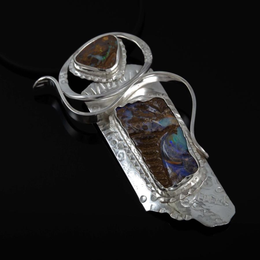 Photograph of a silver pendant featuring  an iridescent opal against black.
