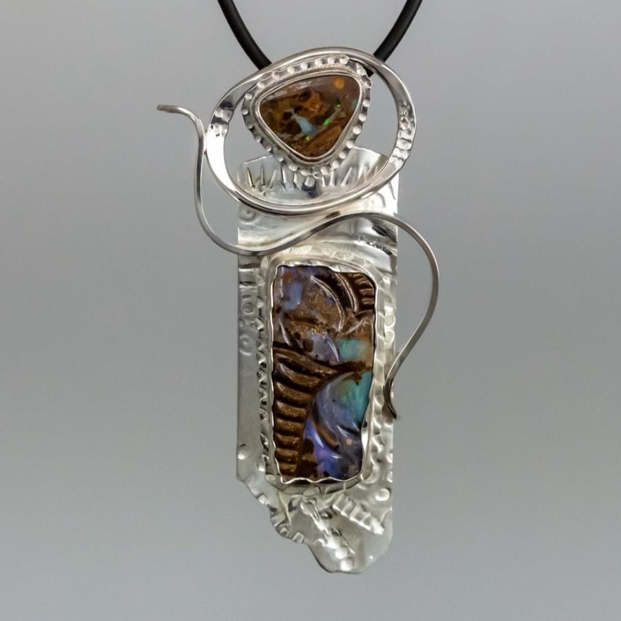 Photograph of a handcrafted silver pendant featuring dark, iridescent opal on a black cord.