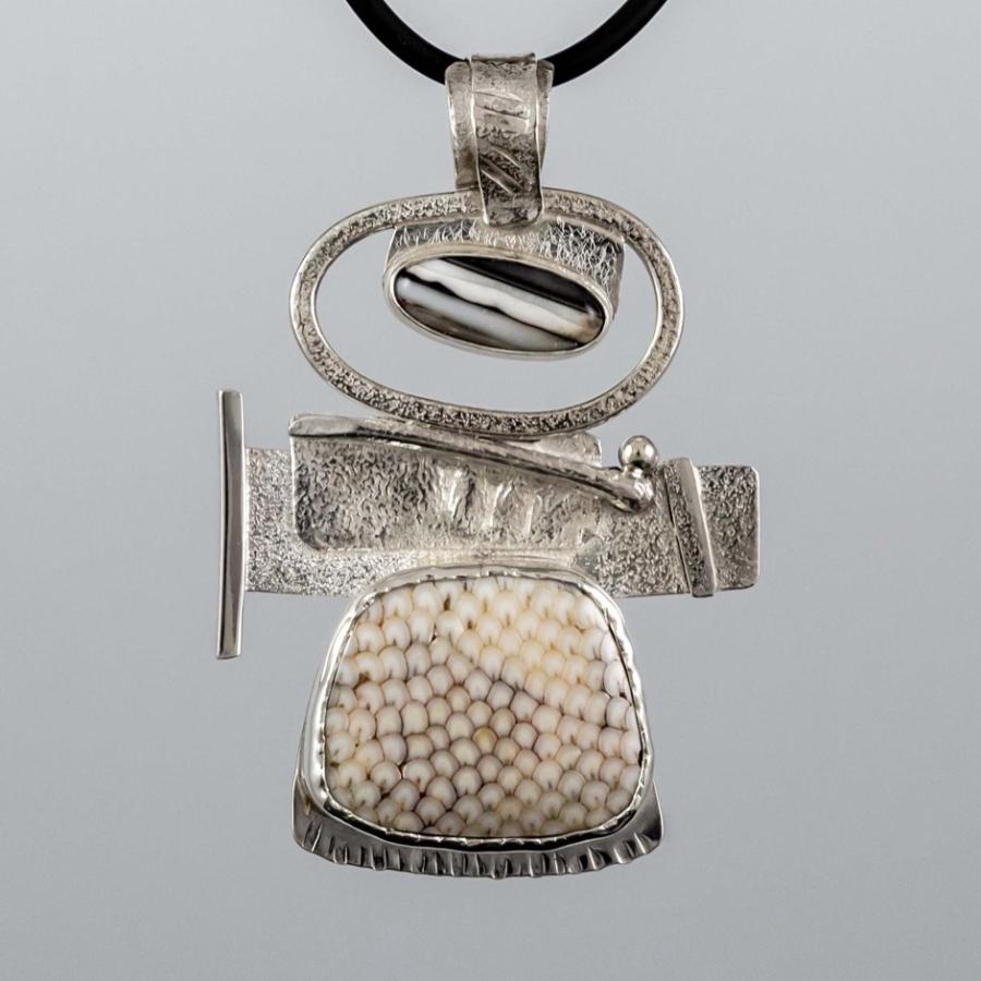 Abstract silver pendant with a patterned stone, suspended on a black cord.