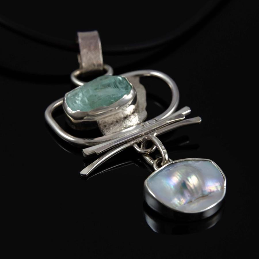 Photograph of a silver pendant featuring a pale green stone and a hanging white pearl.