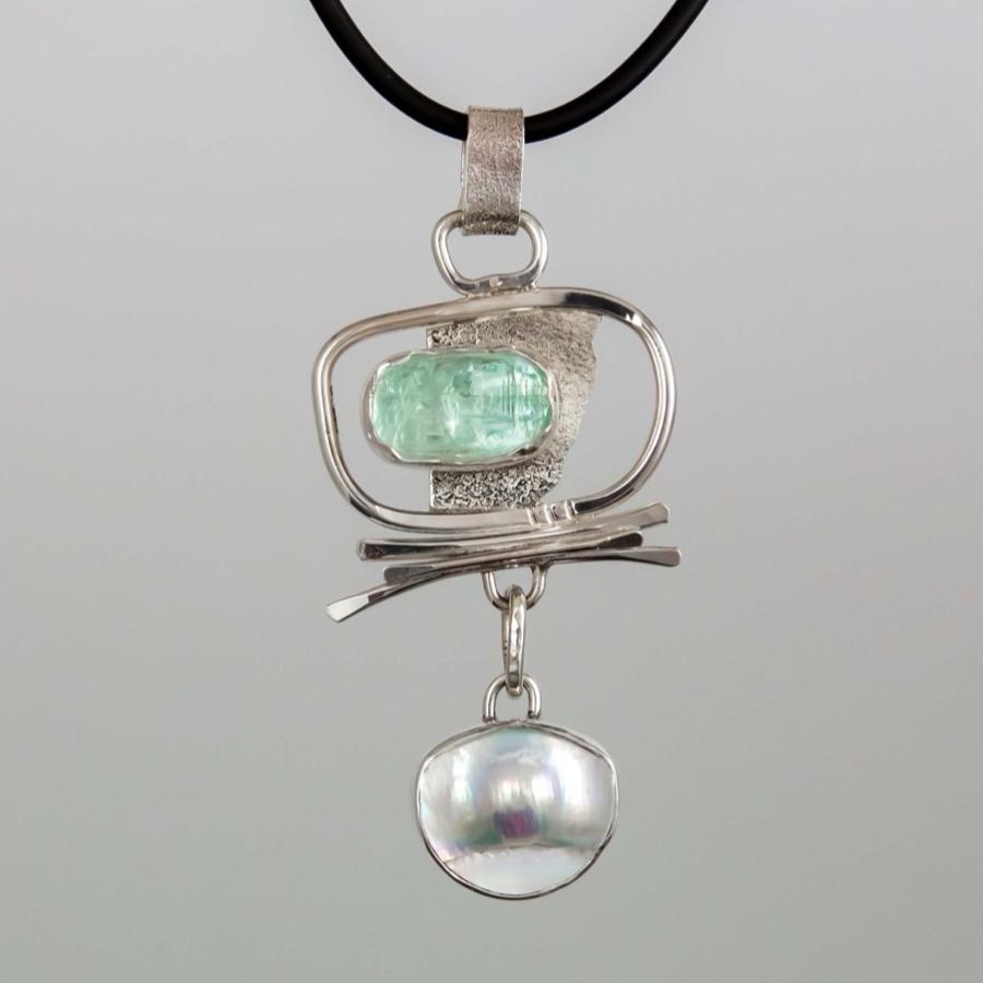 Photograph of a silver pendant on a black cord featuring a green stone and a hanging white pearl.
