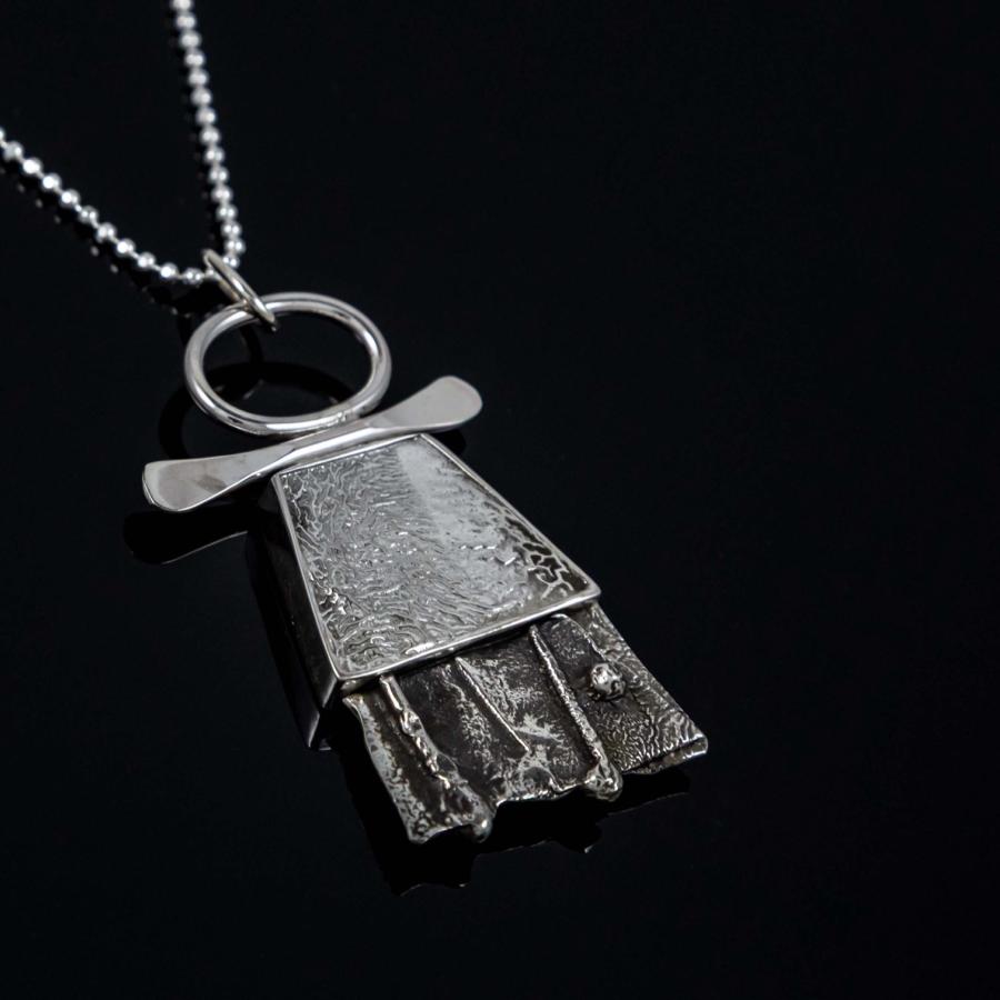 Photograph of a silver textured pendant on a chain against a black background.