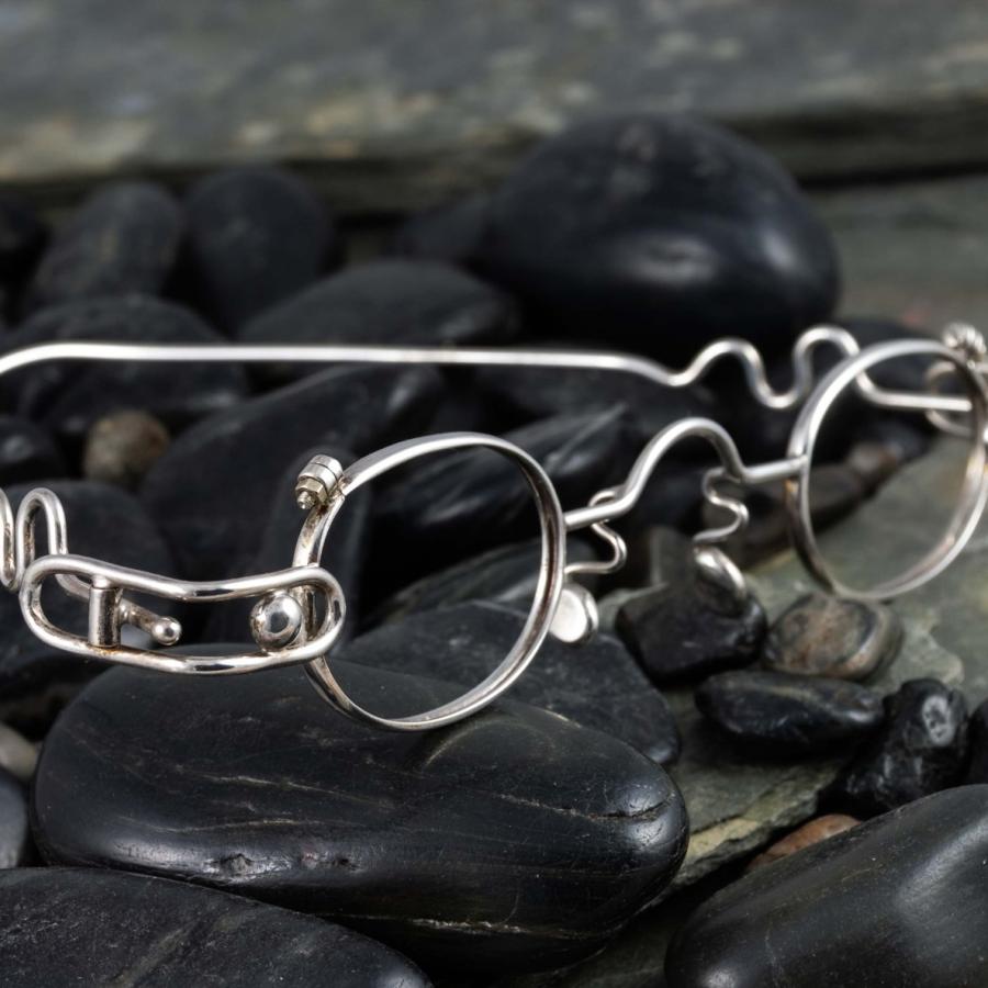 Photograph of handcrafted silver wire-frame glasses resting on dark polished river stones.