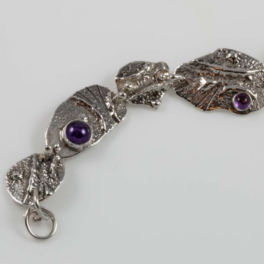 Photograph of a silver link bracelet with ornate leaf-like textures and inset purple gemstones.