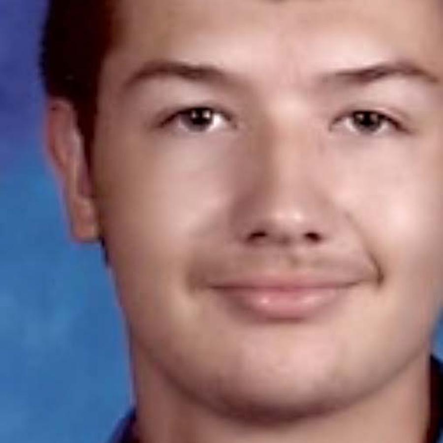 Close-up portrait of a young man with short dark hair against a blue mottled background.