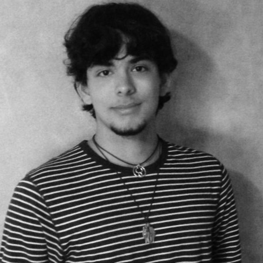 Black and white portrait of a young man with dark curly hair wearing a striped shirt and necklace.