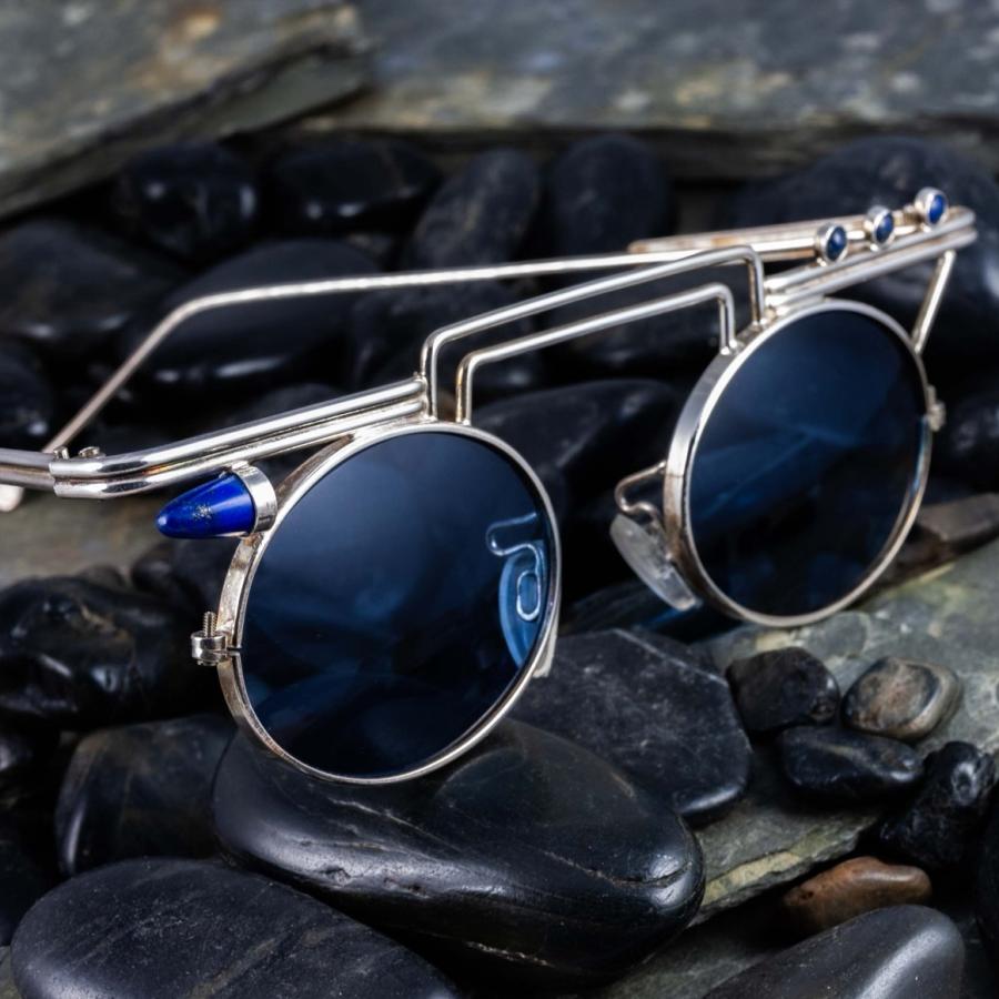 Photograph of avant-garde silver circular sunglasses resting on dark, polished river stones.