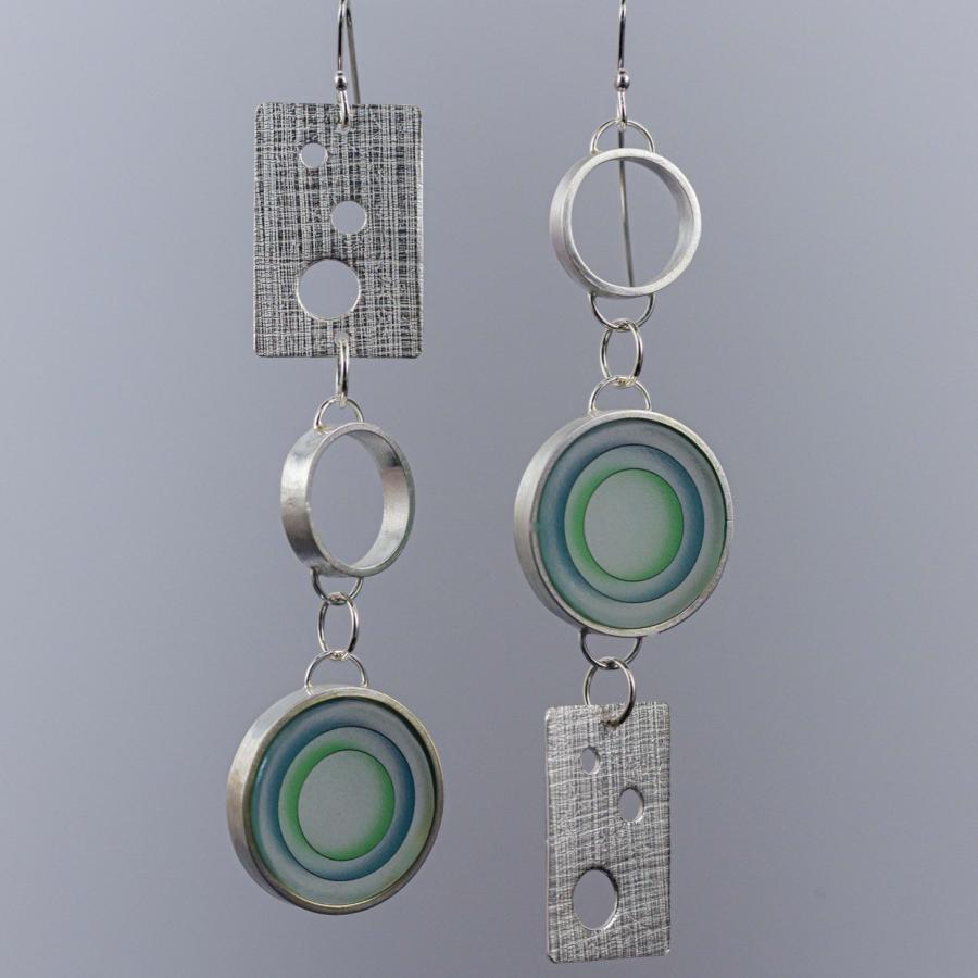 Asymmetrical silver dangle earrings with textured metal rectangles and concentric blue-green glass discs.