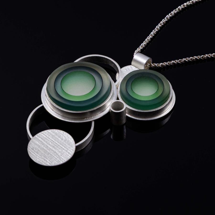 Photograph of a modern silver pendant necklace with green circular inlay on a black background.