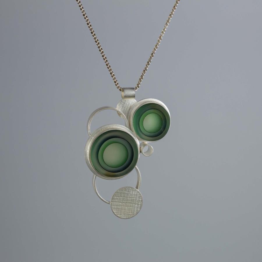 Photograph of a modern silver pendant featuring green glass discs on a thin chain.