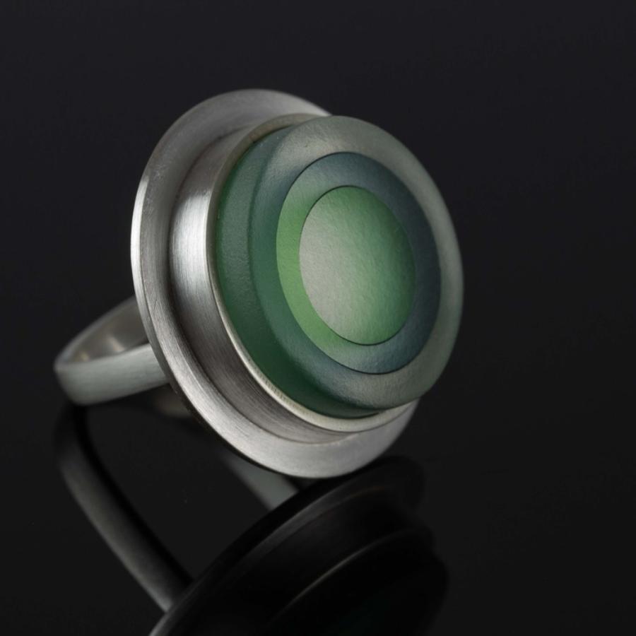 Photograph of a silver ring with a circular, green glass disc on a black surface.