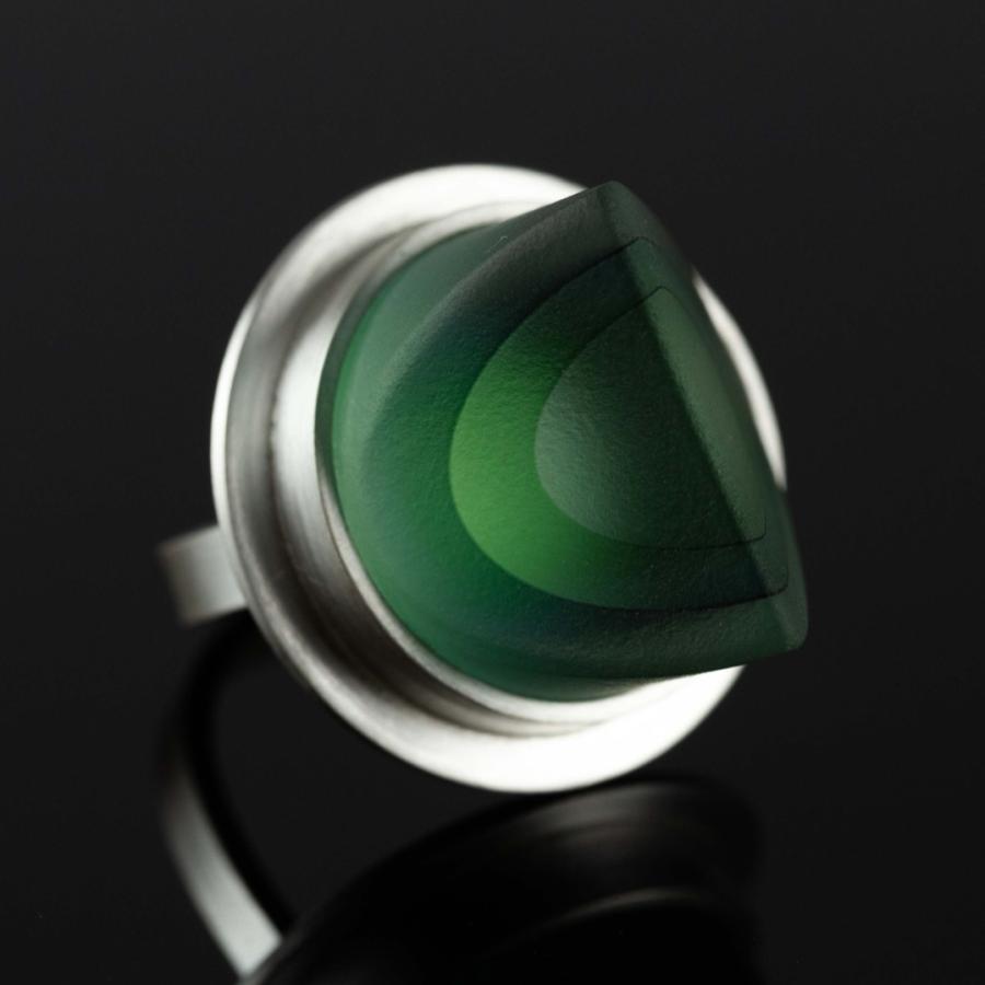 Photograph of a silver ring with a semi-translucent green glass on a dark surface.