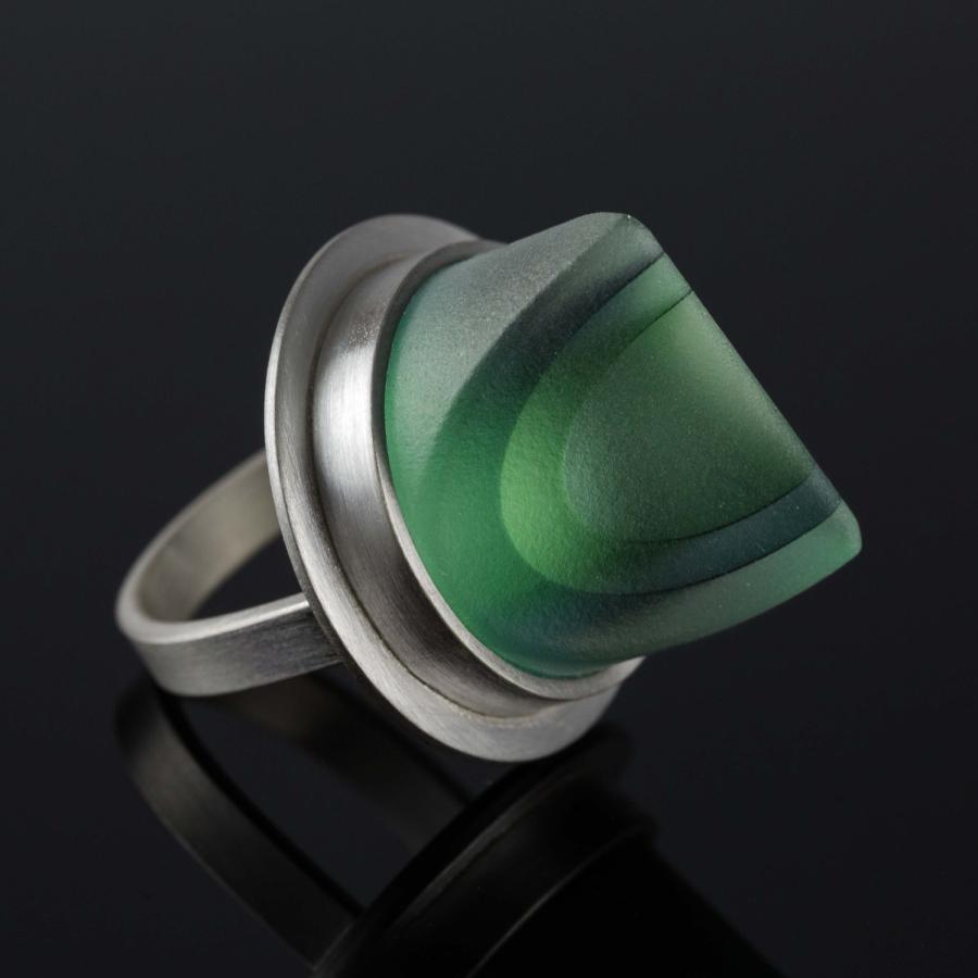 Photograph of a silver ring with a semi-translucent green glass on a dark surface.
