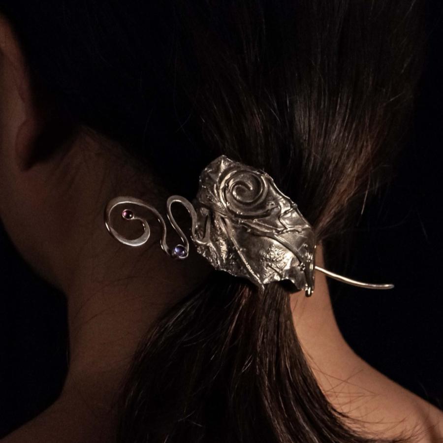 Photograph of a person wearing a decorative, ornate silver hair clip against a black background.