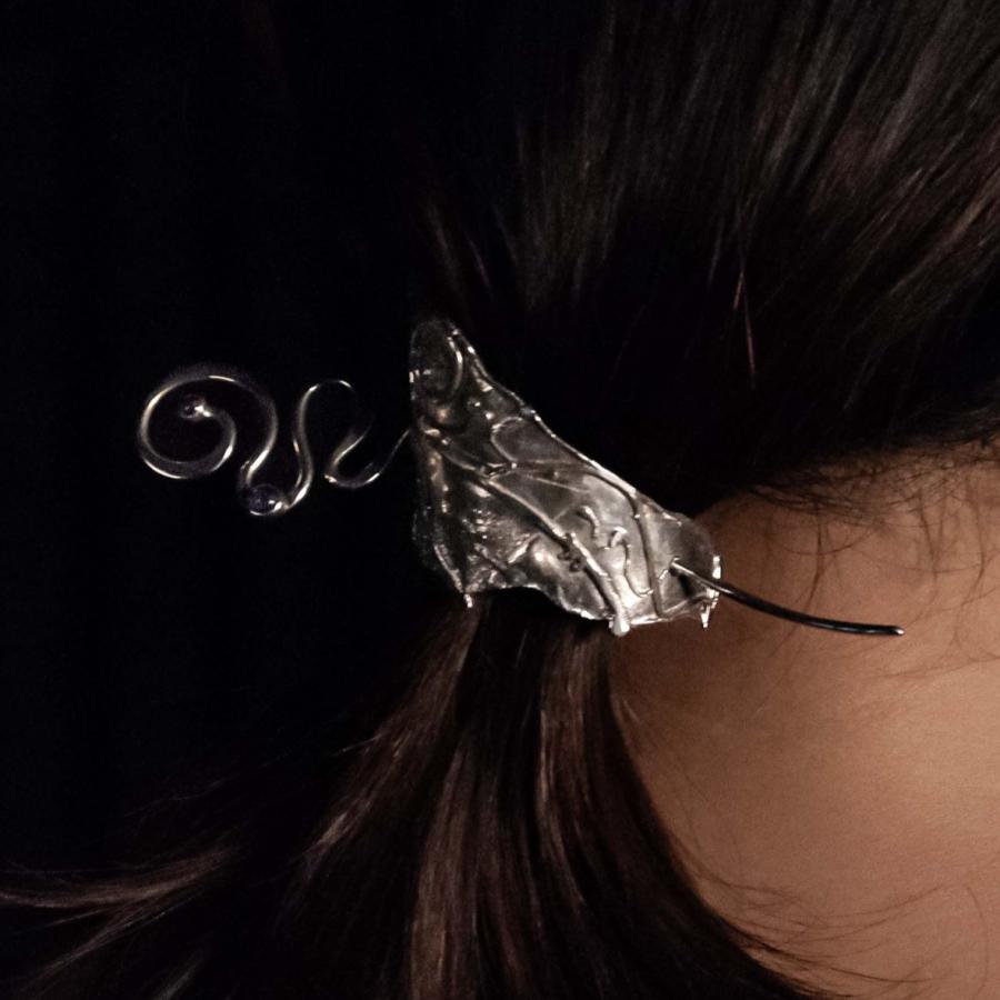 Photograph of a person wearing a decorative, ornate silver hair clip against a black background.