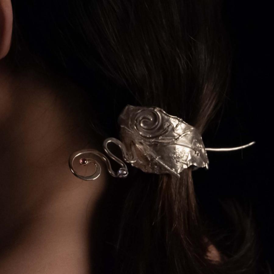 Photograph of a person wearing a decorative, ornate silver hair clip against a black background.