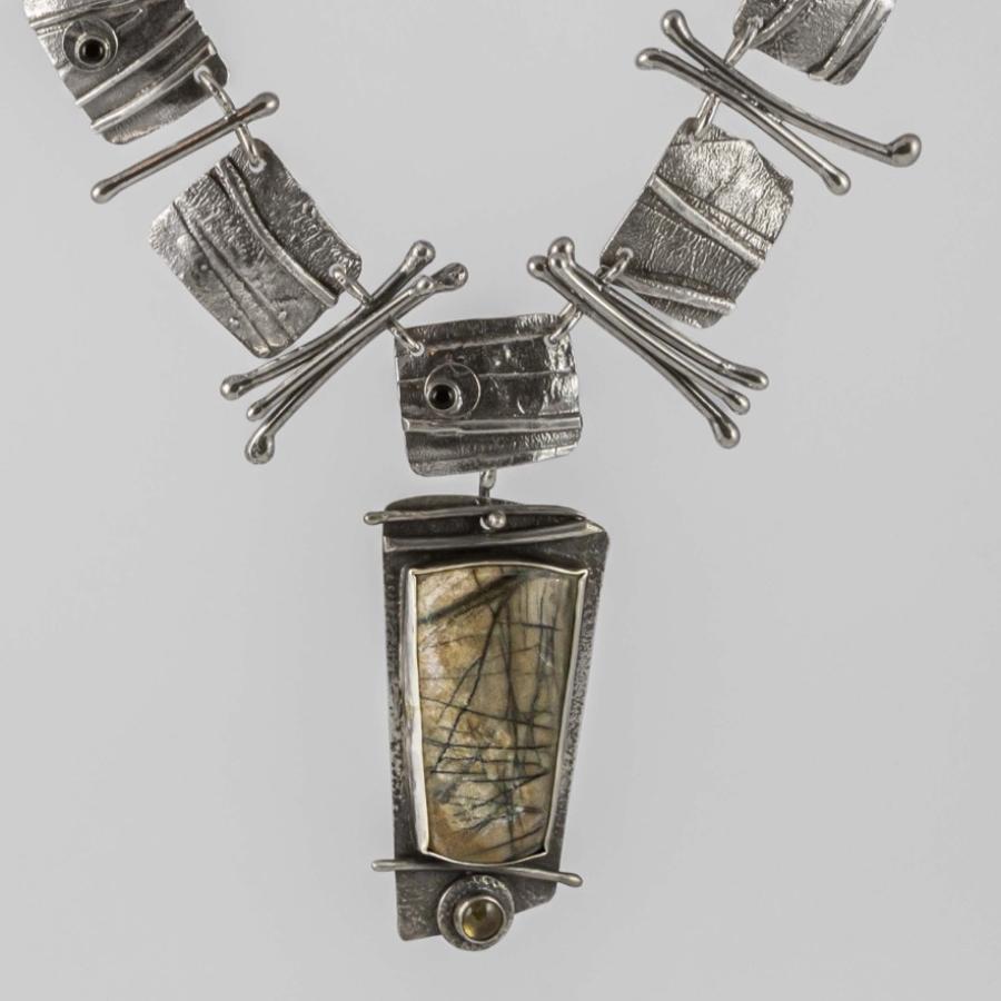 Photograph of a textured silver chain necklace with a central, multi-toned stone pendant.