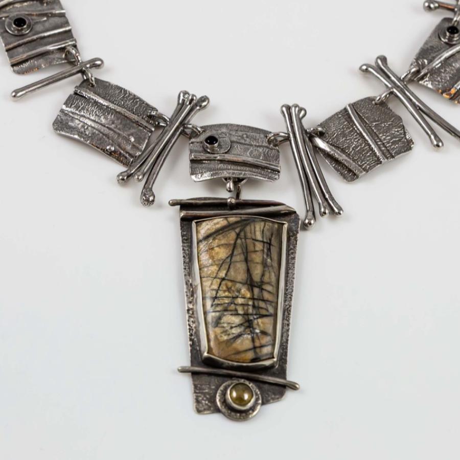 Photograph of a handmade silver necklace with a central abstract stone pendant.