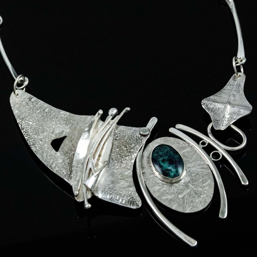 Abstract silver statement necklace with a central blue gemstone on a black background.