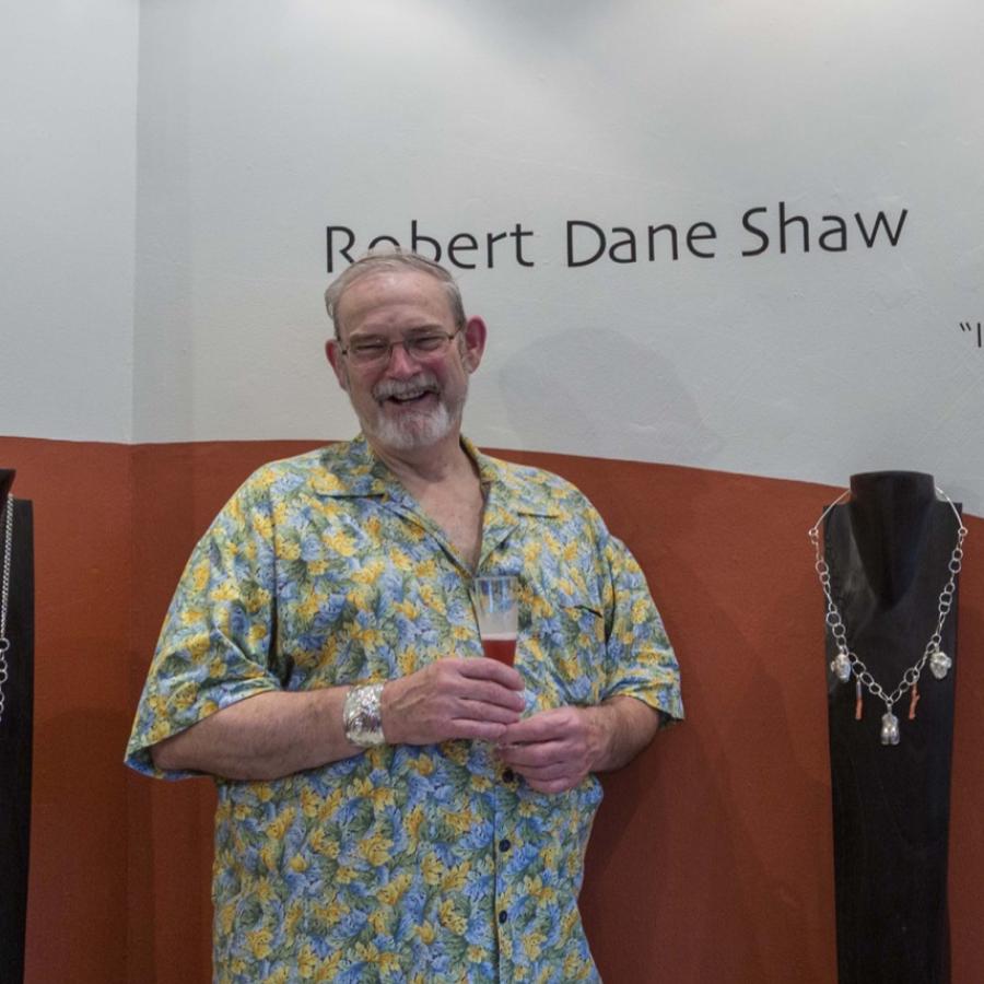 Photograph of a smiling man in a yellow shirt standing next to jewelry displays.