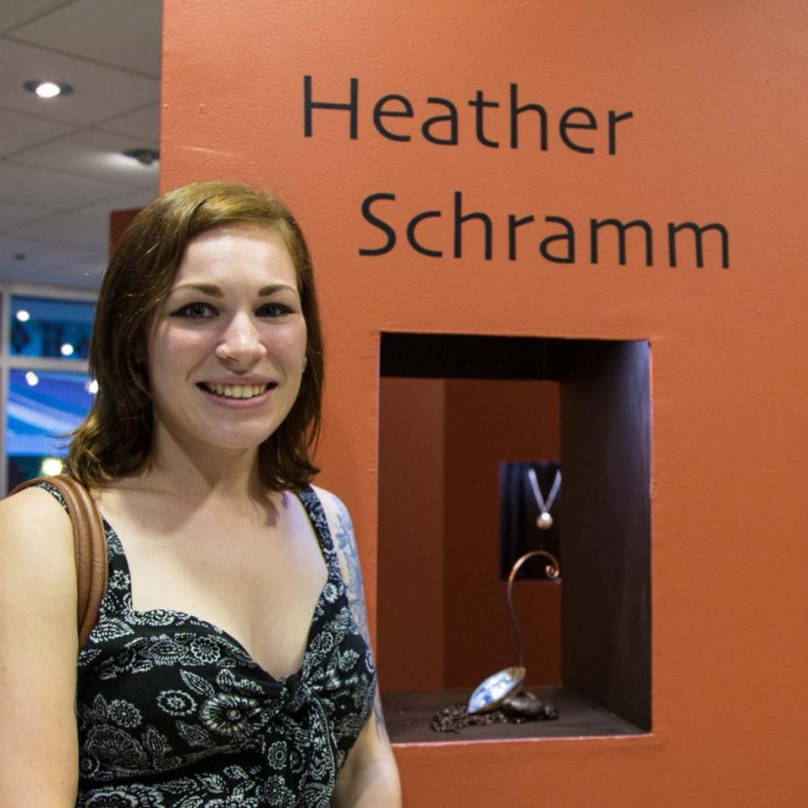 Photograph of a woman smiling, standing beside an orange pillar with the name Heather Schramm.