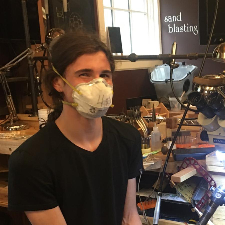 A young person wearing a mask sits in a well-equipped workshop.