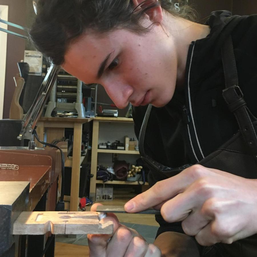 A young person filing metal at a workbench in a brightly lit workshop.
