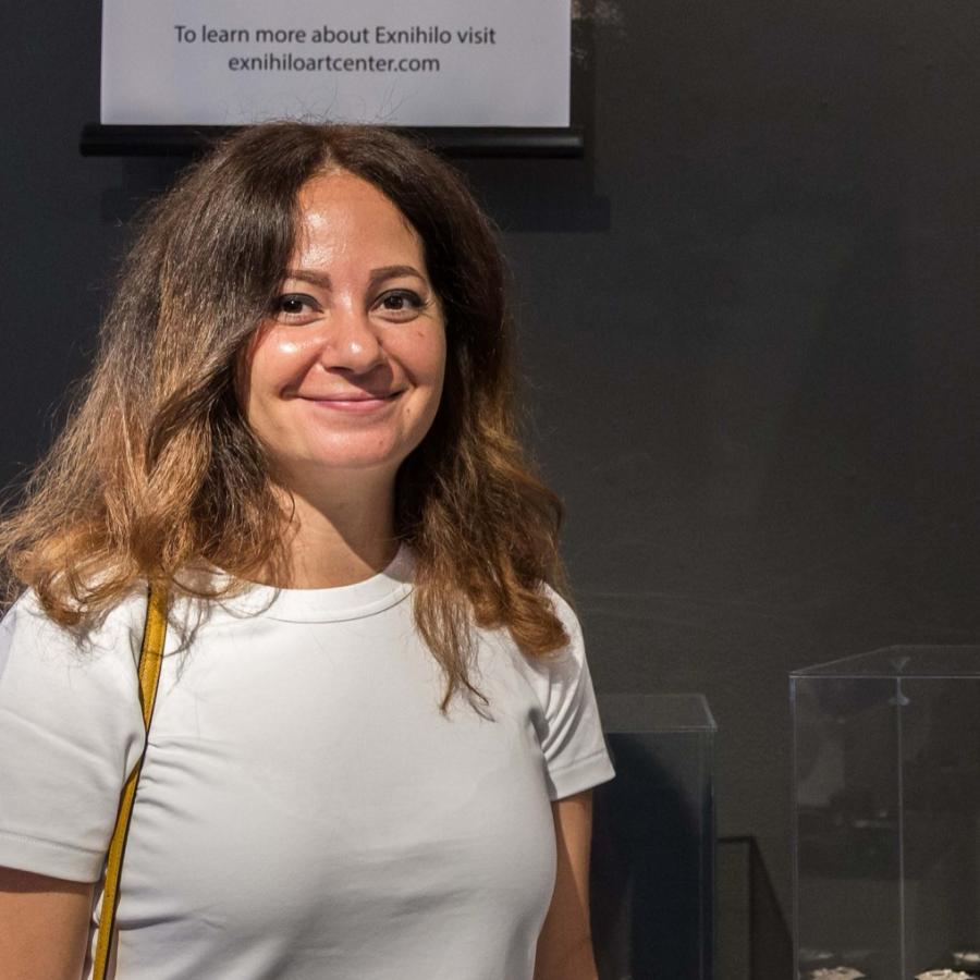 Photograph of a woman smiling in front of an art exhibition wall.