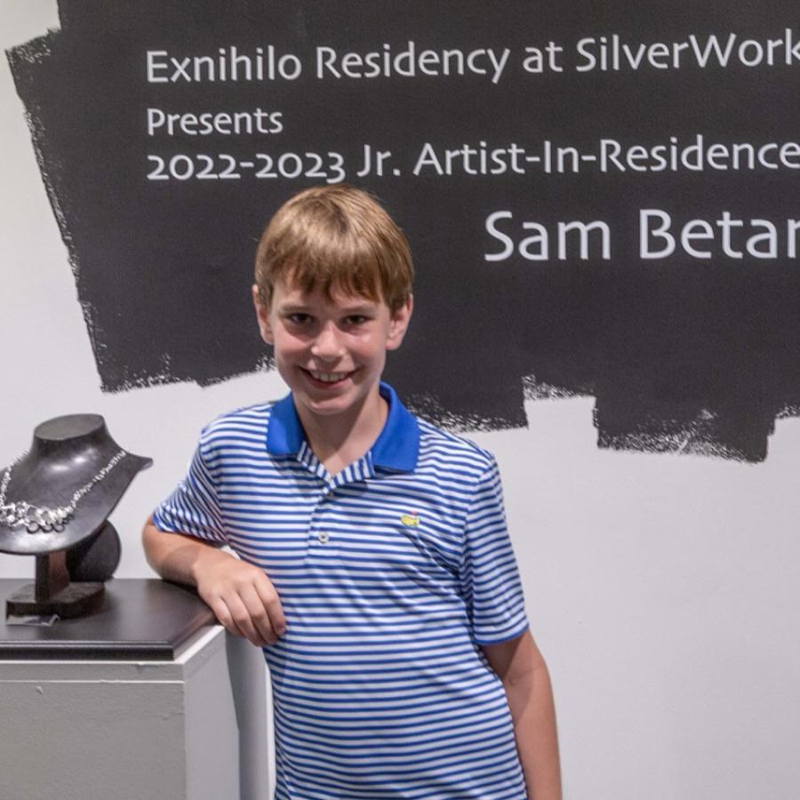 Photograph of a woman and boy smiling next to a pedestal with artwork.